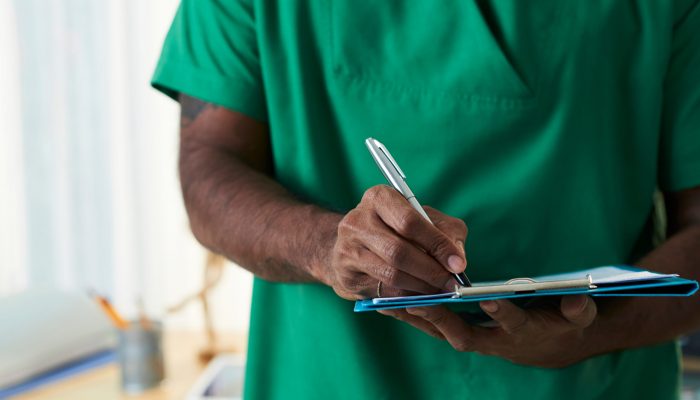 Hand of mixed-race doctor writing down prescriptions or diagnosis on paper while working in clinics